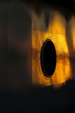 Shadows on a wall, a distorted round porthole window, a net curtain and glowing yellow light.