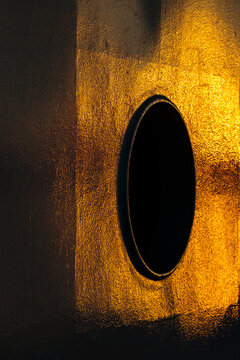 Shadows on a wall, a distorted round porthole window, a net curtain and glowing yellow light.