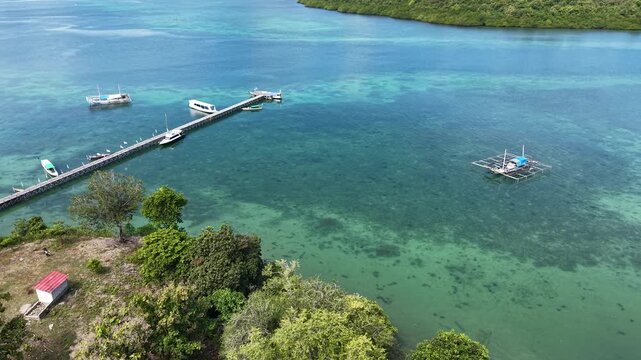 Aerial Drone View of a Tropical Island with Turquoise Clear Water, Wooden Pier, and Boats in East Nusa Tenggara Timur, Indonesia