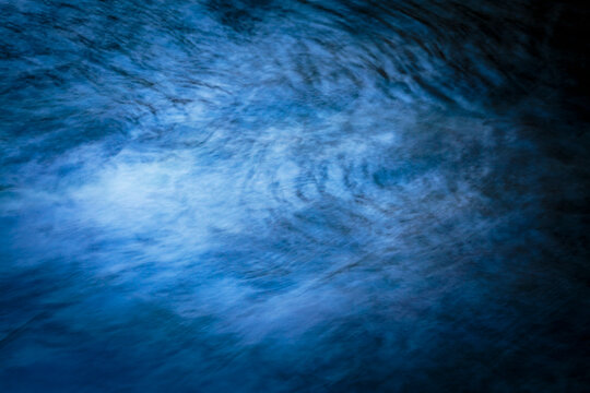Motion blur, flowing water in a river, full frame, graduated deep blue colours.