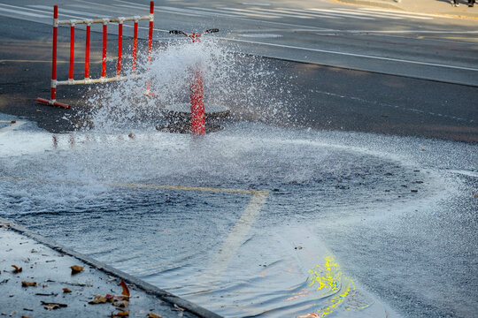 Water spraying from broken fire hydrant flooding city street, red safety barrier in background