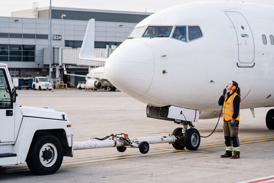 Ground crew member coordinating aircraft pushback with tug at airport gate
