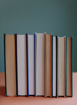 Row of old hardcover books with yellowed pages balancing upright on shelf