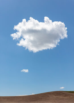 A single shaped cloud with a defined edge against a blue sky above a bare ploughed landscape.
