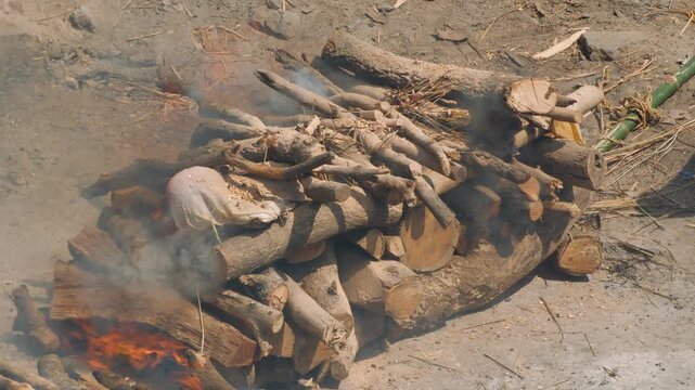 Traditional hindu cremation ceremony taking place on a funeral pyre in varanasi, india. Smoke ascends from the blazing wood as part of a sacred funeral ritual
