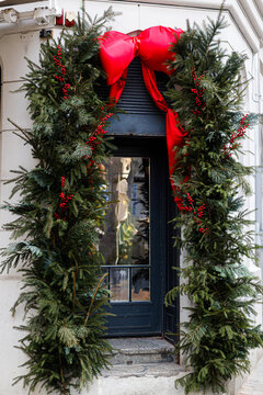 Grand Christmas Doorway Arch Garland with Red Velvet Bow, Evergreen Branches, and Red Holly Berries on Shop Front. Xmas outdoor decor