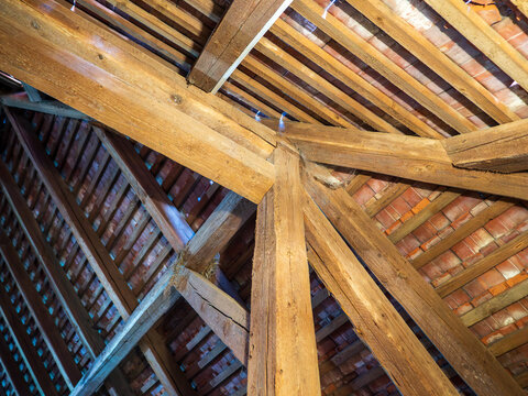 Interior view of a traditional timber roof structure with massive wooden beams, rafters and clay roof tiles. Exposed attic framing illustrating carpentry, architecture and historic construction.