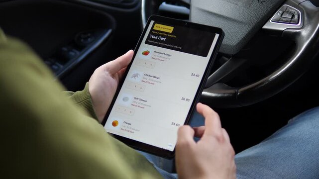 Shopper reviews discounted groceries and sale prices on a tablet in a car, highlighting online shopping, rising food costs, savings and household budgeting.