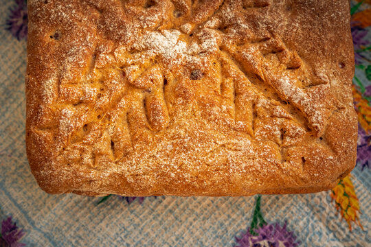 Rustic rectangular homemade bread with a deeply browned crust, delicate flour coating, and decorative branching cuts accented by small baked fruit pieces