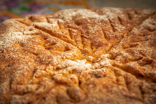 Homemade rustic bread with a deeply golden crust, light flour dusting, and decorative scoring arranged in a striking geometric pattern