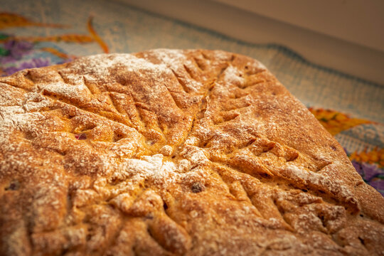 Fresh homemade loaf featuring a golden crust, flour-dusted surface, and distinctive decorative scoring with small baked fruit pieces scattered across the bread
