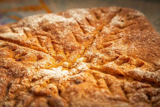 Golden brown homemade bread with a crisp crust and decorative radial cuts, lightly dusted with flour and baked into a distinctive geometric shape