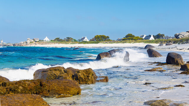 Ocean waves crashing on rocky sandy beach with coastal village in Meneham Kerlouan Brittany France