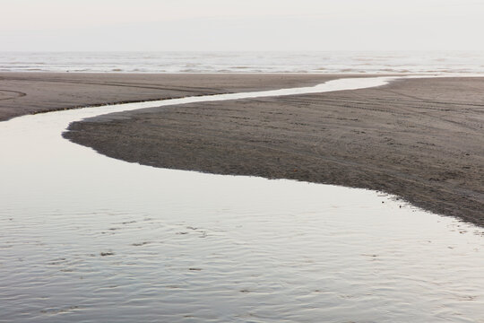 A curving stream flows across a beach into the ocean at dusk.