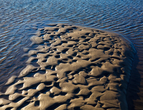 Beach sand formations, created by water action, ripples and ridges, patterns, shallow water and an incoming tide.