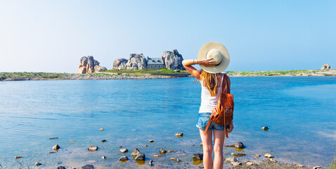 Young female traveler with straw hat and backpack looking at famous house between rocks in Castel Meur Plougrescant Brittany France © M.studio