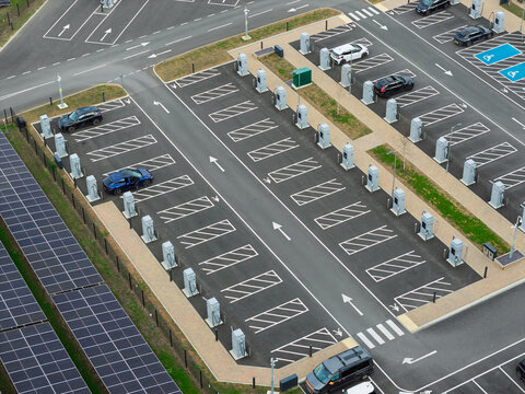 Aerial view of an electric vehicle charging station with multiple charging points, parked cars, and solar panel arrays in the United Kingdom.