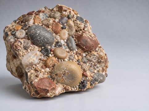 Close-up of a conglomerate rock specimen showing rounded pebbles cemented together in a matrix of sand and gravel, a sedimentary geological stone with rough texture, isolated on a neutral grey