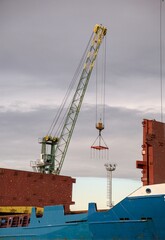 Lattice boom harbor crane lowering cargo spreader rig above ship holds. © YuliiaKettu