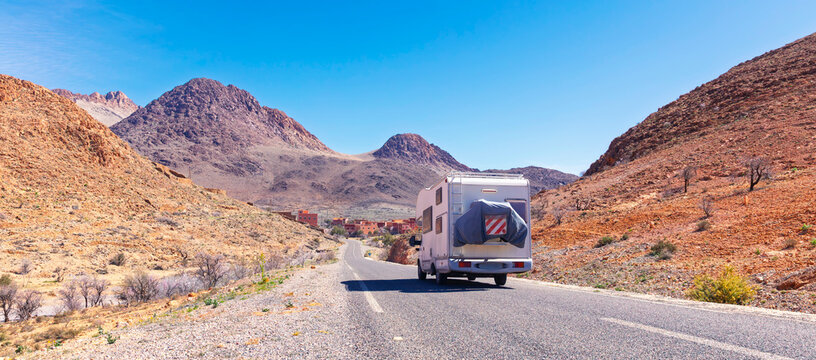 Camper van driving on asphalt road through arid desert mountain landscape in Anti Atlas Morocco