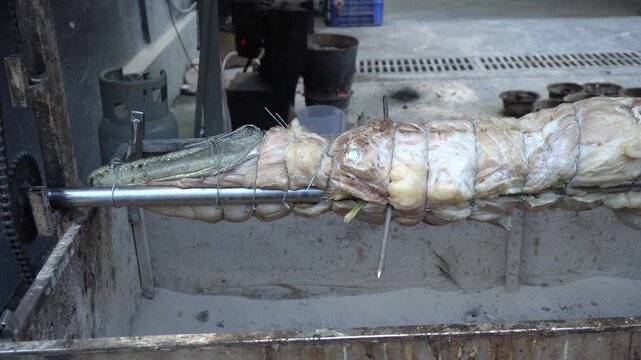 A tied meat roast turns on a metal rotisserie spit