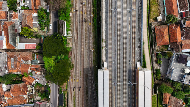 Aerial view of Stasiun KCIC Padalarang with its parallel railway tracks, platforms, and surrounding residential neighborhood with terracotta rooftops in Kecamatan Padalarang, Jawa Barat, Indonesia.