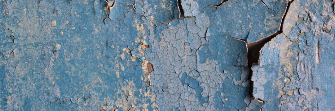 Peeling paint on the wall. Panorama of a concrete wall with old cracked flaking paint. Weathered rough painted surface with patterns of cracks and peeling. Wide panoramic texture for design background