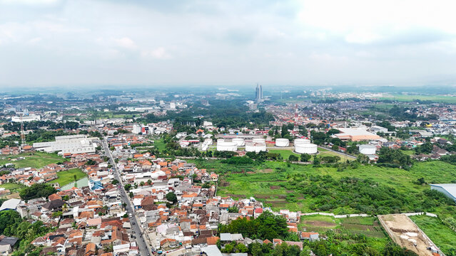 Aerial view of residential rooftops, industrial storage tanks, and green fields in Ngamprah, West Java, Indonesia.