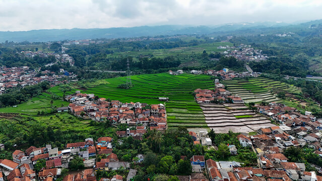Aerial view of the village of Ngamprah surrounded by lush green rice terraces and rolling hills in Ngamprah, West Java, Indonesia.