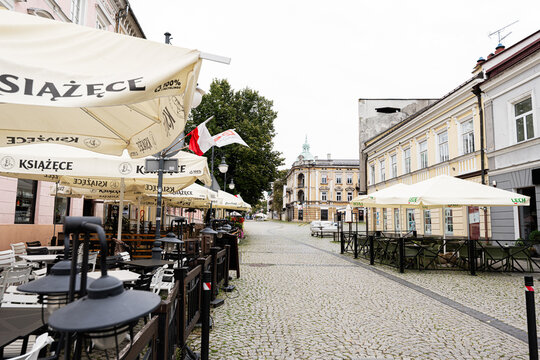 Outdoor caf&eacute; terraces and pedestrians along a historic cobblestone street in Radom, Poland with umbrellas and classic town architecture