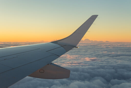 Aerial view of an airplane wing flying above a thick layer of clouds during golden hour in Hessen, Germany.