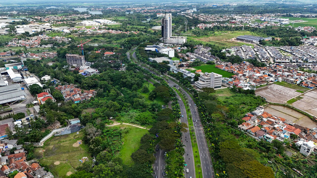 Aerial view of Kota Baru Parahyangan featuring a highway, modern residential developments, lush greenery, and a high-rise building in Kecamatan Padalarang, Jawa Barat, Indonesia.