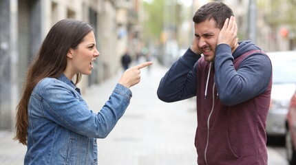 Fototapeta premium A woman angrily points her finger and yells at a man who covers his ears during a street argument.