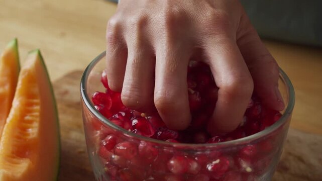 hand grabing a handful of fresh ruby-red pomegranate arils from a clear glass bowl