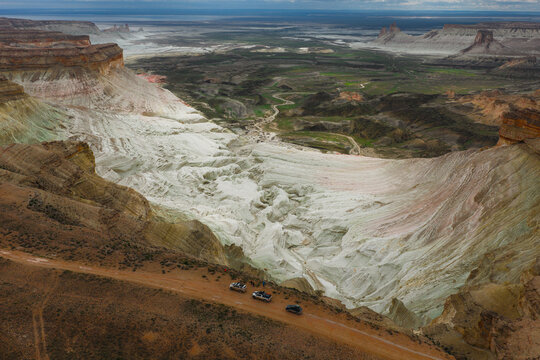 Aerial view of the dramatic white limestone cliffs and desert landscape of Bozjyra with off-road vehicles driving on a dirt road in Aktau, Mangystau Region, Kazakhstan.