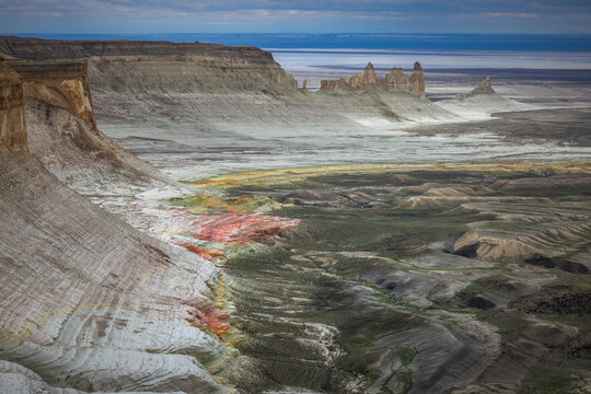 Aerial view of the dramatic limestone cliffs and unique rock formations of Bozjyra, showcasing colorful sedimentary layers and vast desert plains in Aktau, Mangystau Region, Kazakhstan.