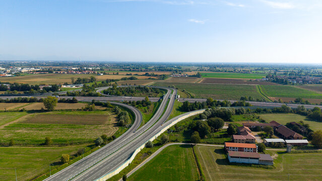 Aerial view of the A58 TEEM motorway interchange featuring modern highway infrastructure, surrounding agricultural fields, and rural landscape in Liscate, Lombardy, Italy.