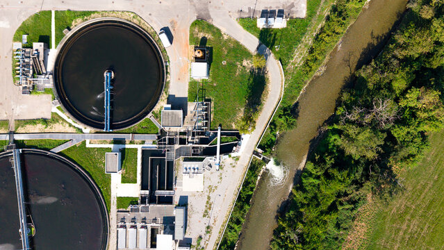 Aerial view of Depuratore di Truccazzano with circular sedimentation tanks and water treatment infrastructure next to a river and green fields in Truccazzano, Lombardia, Italy.