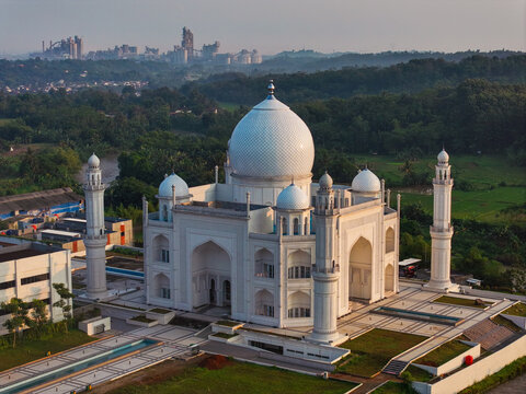 Aerial view of Budi Guna Mosque with its white dome and minarets, surrounded by lush green landscape and industrial buildings in Citeureup, West Java, Indonesia.
