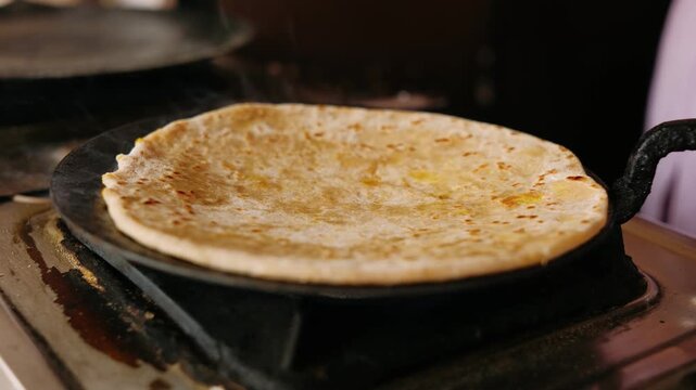 Traditional indian paratha bread on a hot tawa pan. Preparing stuffed aloo paratha with ghee for breakfast