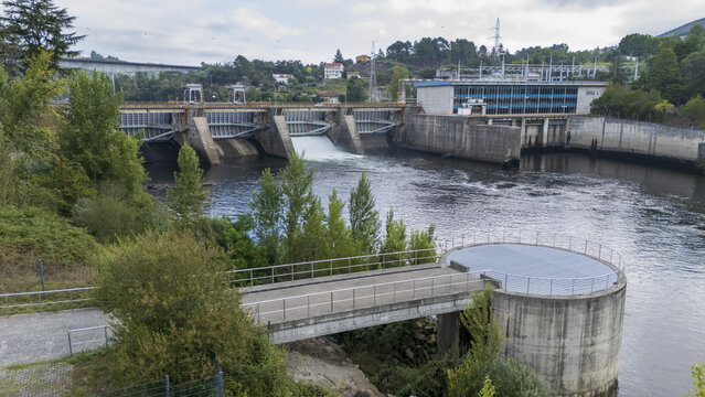 Aerial view of Subestacion Electrica Velle and the Velle Dam on the Mino River, featuring concrete structures, flowing water, and surrounding lush greenery in Ourense, Ourense, Spain.