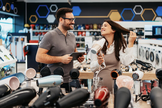 Retail shopping experience featuring a smiling sales assistant with a tablet helping an expectant mother select home appliances in a consumer electronics store.