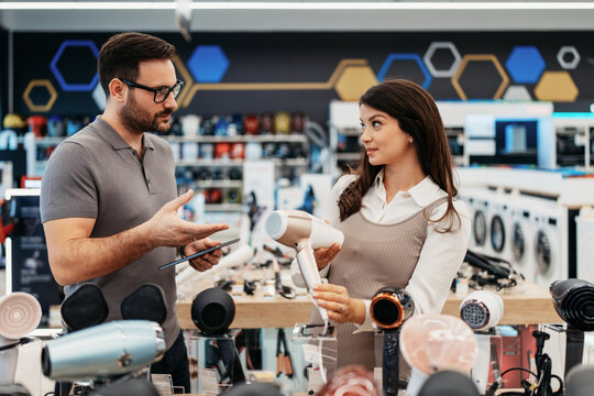 Retail shopping experience featuring a smiling sales assistant with a tablet helping an expectant mother select home appliances in a consumer electronics store.