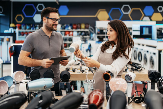 Retail shopping experience featuring a smiling sales assistant with a tablet helping an expectant mother select home appliances in a consumer electronics store.