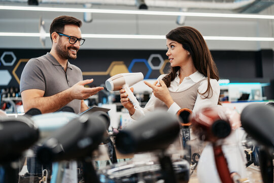 Friendly store clerk consulting with an expectant mother holding a modern hair styling device while browsing home appliances in a well-lit retail showroom.