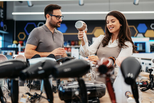 Friendly store clerk consulting with an expectant mother holding a modern hair styling device while browsing home appliances in a well-lit retail showroom.