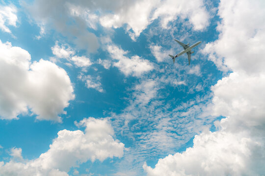 Passenger jet flying through a blue sky with scattered white clouds, with two engines beneath swept wings and a long fuselage ending in a blue tail.