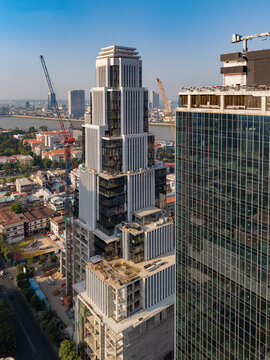 Aerial view of a modern skyscraper under construction featuring multiple cranes, glass facade elements, and surrounding urban landscape, Phnom Penh, Cambodia.