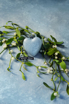 Christmas holiday concept. beautiful mistletoe plant branch with decorative glittering heart and text "Merry Xmas" on blue-gray background. decor for Christmas, Advent, festive winter season.