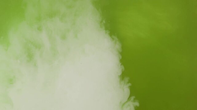 Milk pouring into green matcha tea creates flowing white clouds and swirling patterns. Macro view of liquid blending during matcha latte preparation, forming abstract background with green gradient.